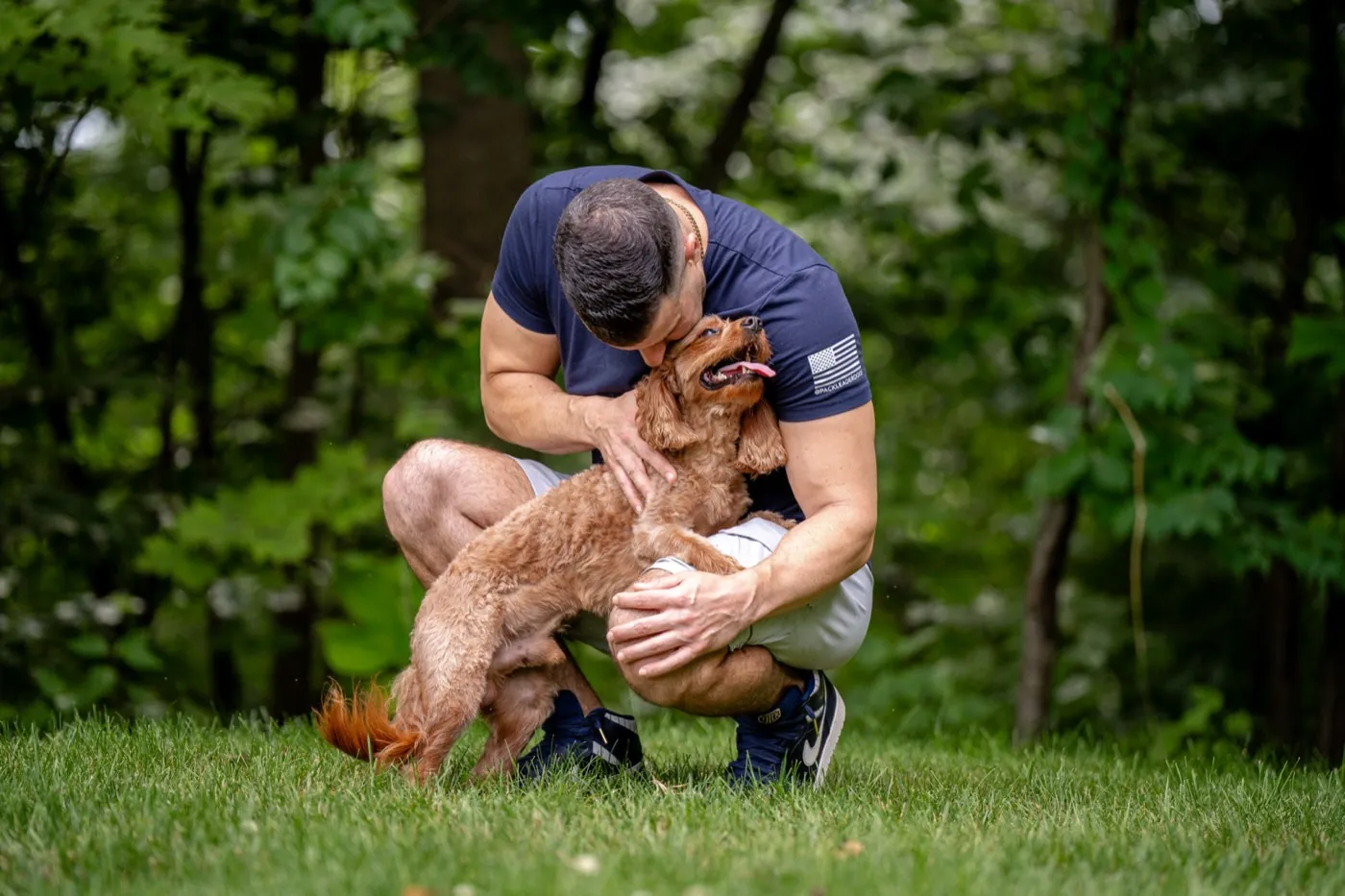 Steve Del Savio crouched in the grass, nuzzling a young cavapoo standing into his arms.