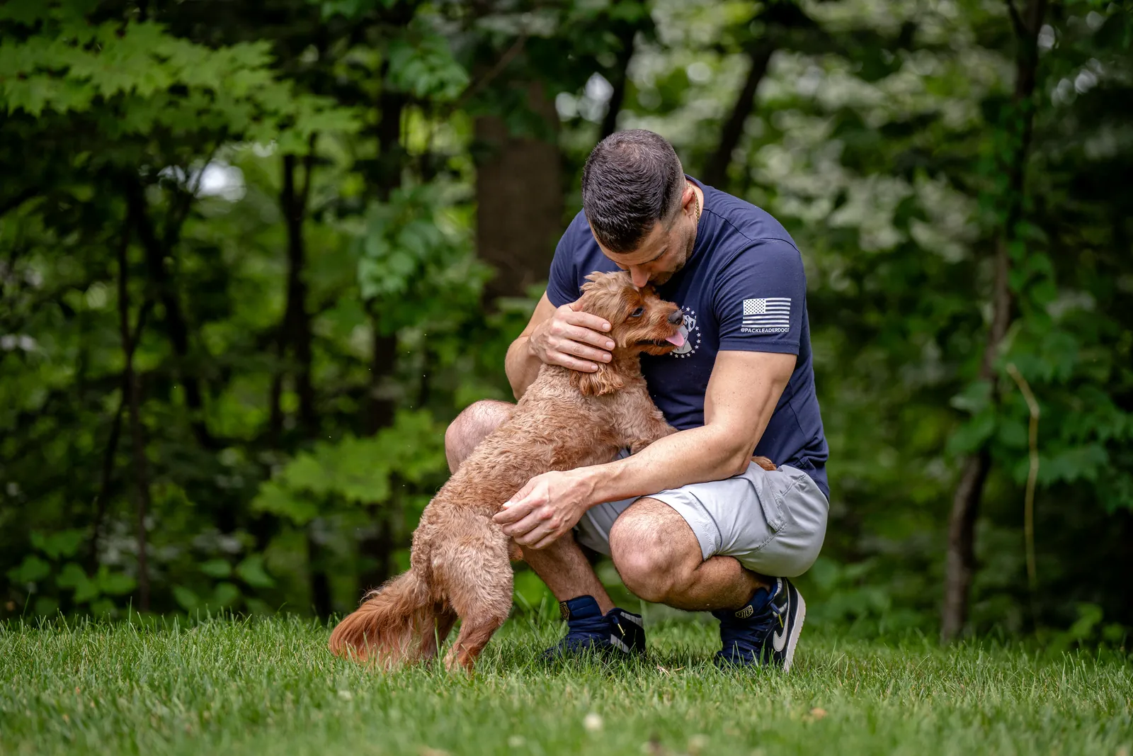 Steve Del Savio crouched in the grass with a young cavapoo in his arms.